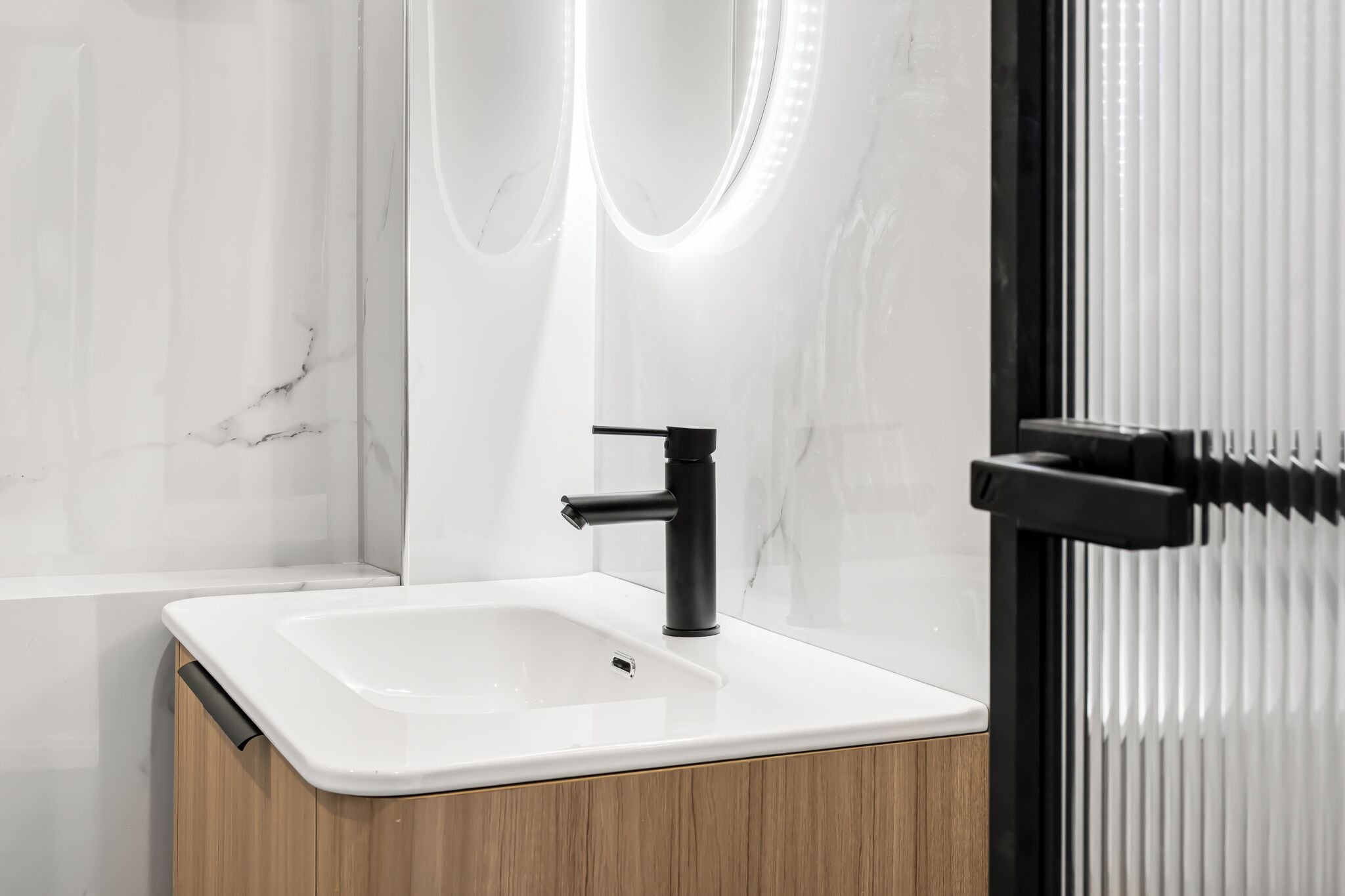 A modern bathroom with a white sink, black faucet, and wooden cabinet.