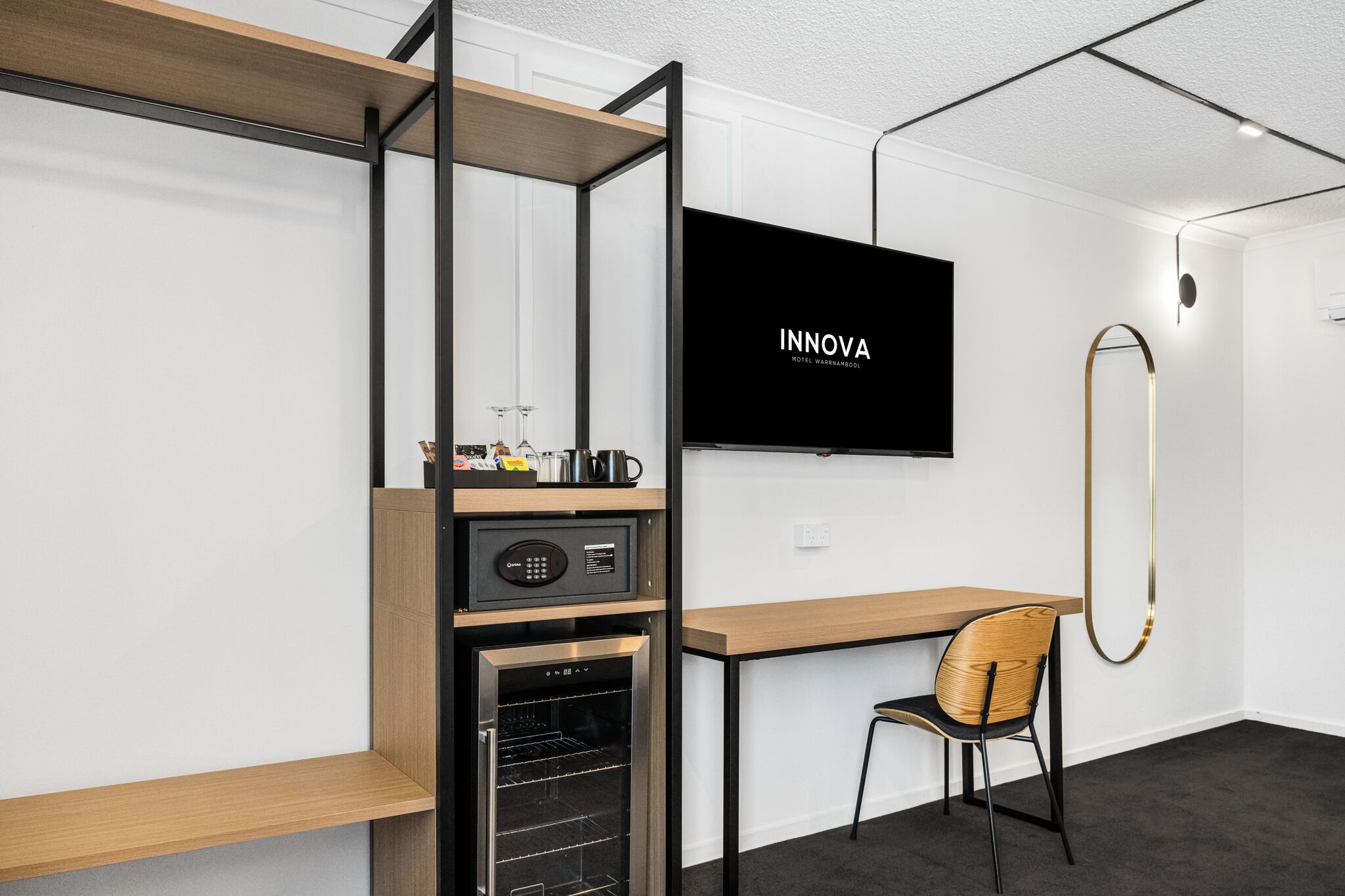 A modern hotel room with a wooden desk, a television, a minibar, and a compact refrigerator.