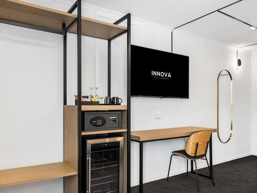 A modern hotel room with a wooden desk, a television, a minibar, and a compact refrigerator.
