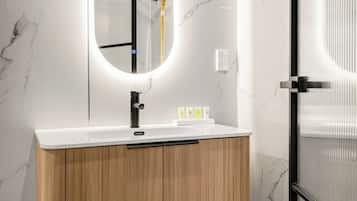 A modern bathroom with a marble wall, a wooden vanity, a sink with a black faucet, and a mirror with a circular light.