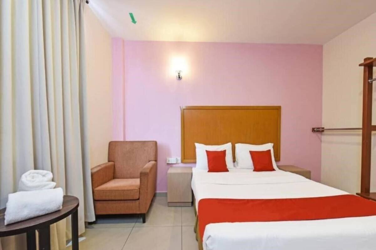 A hotel room with a bed, a chair, a nightstand, a lamp, and a window with curtains.