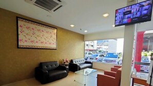 Un hall de hotel con una gran obra de arte floral, un televisor de pantalla plana y zonas de estar, incluyendo un sofá negro y sillas rojas.