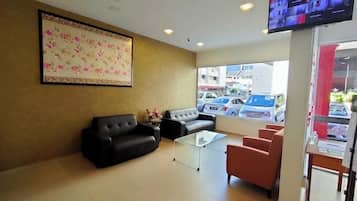Eine Hotelhalle mit einem großen floralen Kunstwerk, einem Flachbildfernseher und Sitzbereichen, darunter eine schwarze Couch und rote Stühle.