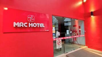 The exterior of MRC Hotel with a red facade, glass entrance, and a no-smoking sign.