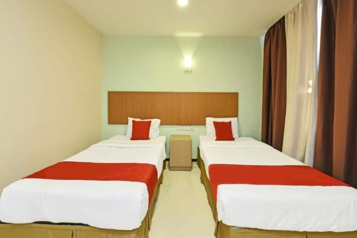 A hotel room with two single beds, a wooden headboard, a small bedside table, and a window with curtains.