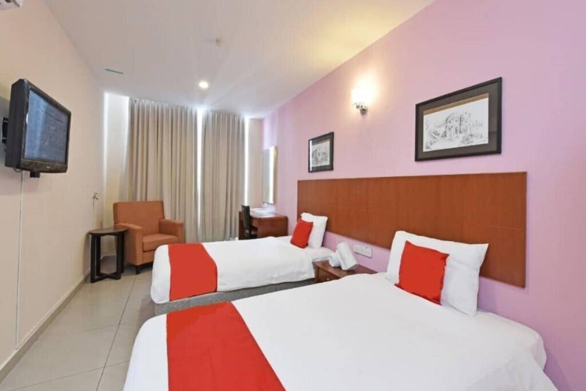 A hotel room with two beds, a television, a chair, and a desk with a lamp.