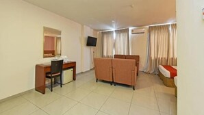 Habitación de hotel con escritorio, silla, sofá y televisor montado en la pared.