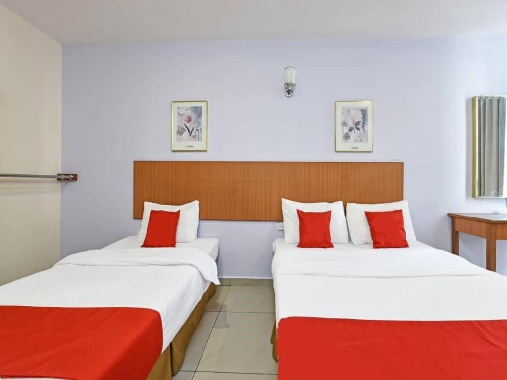 A hotel room with two beds, each with white bedding and red accents, a wooden headboard, and two framed pictures on the wall.