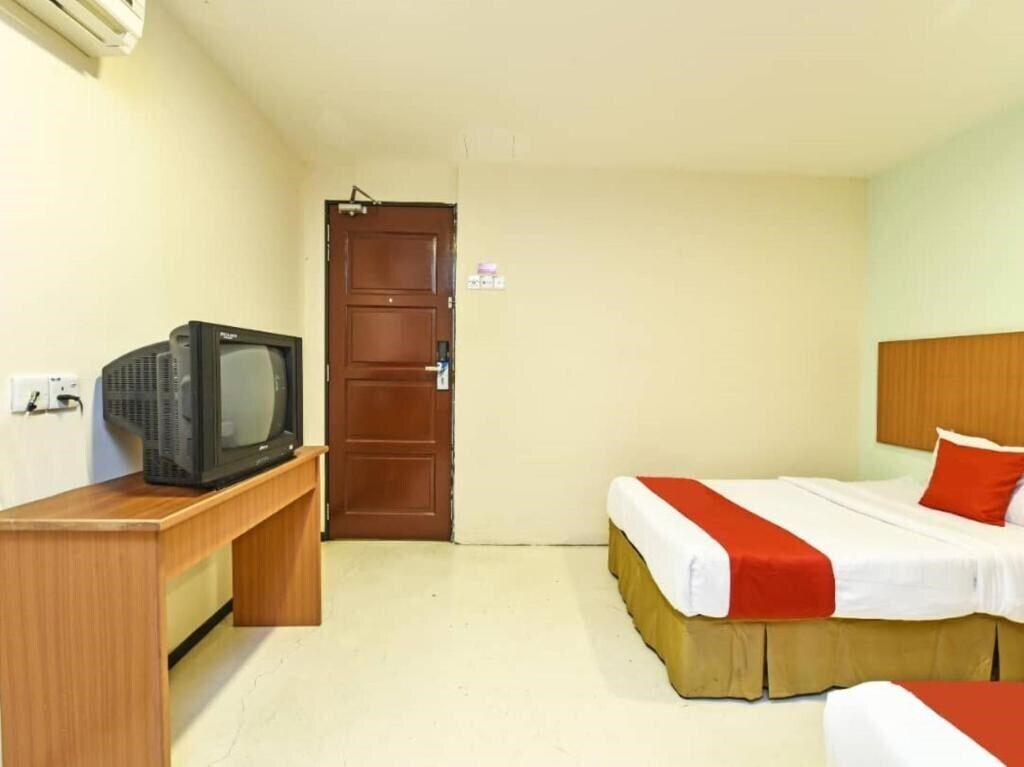 A hotel room with a bed, a TV on a wooden stand, and a door.