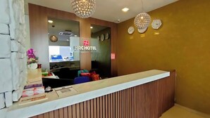 Un espace d’accueil d’hôtel au design moderne, comprenant un comptoir d’accueil, une horloge et un luminaire décoratif.