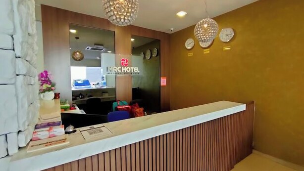 Zona de recepción de hotel con diseño moderno, que incluye un mostrador de recepción, un reloj y un elemento de iluminación decorativo.