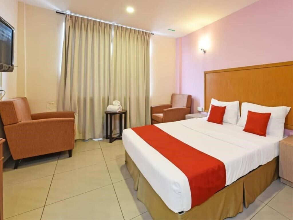 A hotel room with a large bed, two armchairs, a small table, and a TV.