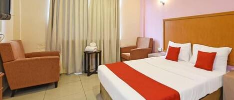 A hotel room with a large bed, two armchairs, a small table, and a TV.