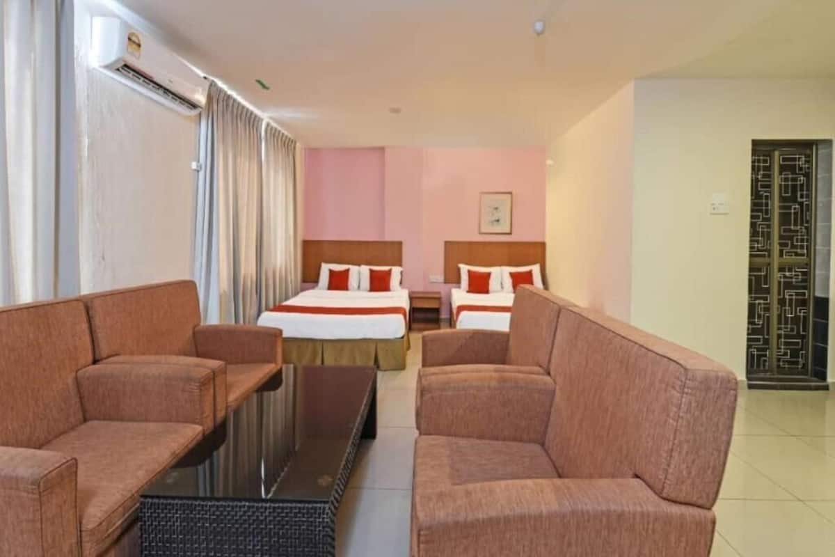 A hotel room with two beds, a sofa, a small table, and an air conditioning unit.