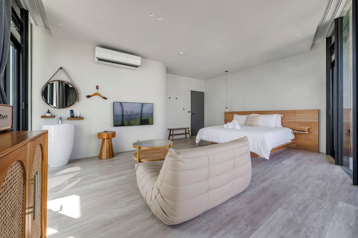 A modern hotel room with a bed, a sofa, a desk, and a TV.