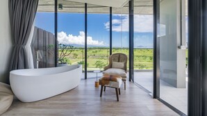 A modern bathroom with a freestanding bathtub, a chair, and a view of a green landscape through large glass doors. - Ningxialight (Wujie)