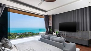 Une chambre moderne avec un grand lit, un canapé, une télévision et un balcon offrant une vue sur l’océan.