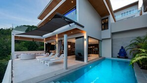 Une maison moderne dotée d’une piscine, d’un espace salon extérieur et d’une statue de Bouddha.