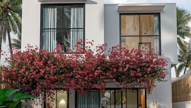 Een modern, twee verdiepingen hoog gebouw met een zwembad, grote ramen en een balkon beplant met bloeiende planten.