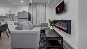 A modern living room with a grey sofa, a coffee table, and a flat-screen TV mounted on the wall. - St. Albert Luxury New 2BR/2BA Basement • Private Entrance • Pet-Friendly (St. Albert)