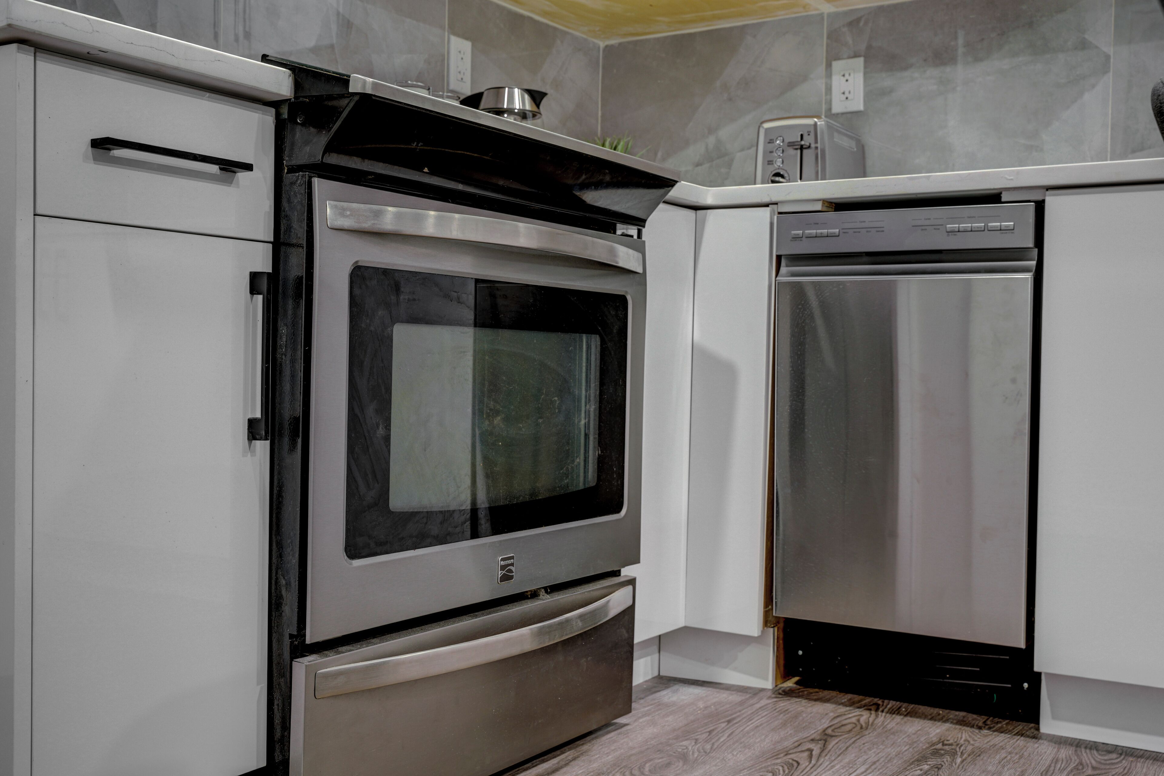 Una cocina moderna con electrodomésticos de acero inoxidable, incluyendo un horno y un lavavajillas, y armarios blancos.