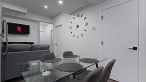 A modern living room with a glass dining table, grey sofas, and a wall clock. - St. Albert Luxury New 2BR/2BA Basement • Private Entrance • Pet-Friendly (St. Albert)