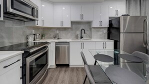 A modern kitchen with white cabinets, stainless steel appliances, and a glass dining table. - St. Albert Luxury New 2BR/2BA Basement • Private Entrance • Pet-Friendly (St. Albert)