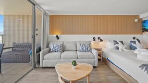 Una habitación de hotel moderna con sofá, cama, una mesita de madera y vistas al exterior.