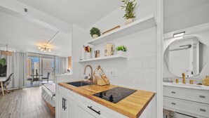Una cocina moderna con armarios blancos, encimera de madera y estufa empotrada. Hay estantes sobre el lavabo con utensilios de cocina y plantas.