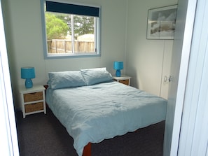 Une chambre à coucher avec un lit, deux tables de chevet, une fenêtre et une porte.