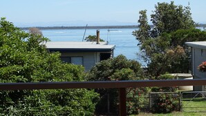 Zona residencial con vista a una extensa masa de agua, posiblemente un lago o el mar, con montañas al fondo. Se observan casas con tejados visibles y una cerca en primer plano.