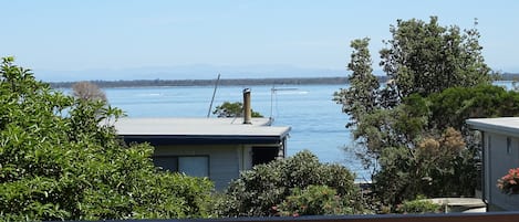A residential area with a view of a large body of water, likely a lake or sea, with mountains in the distance. There are houses with visible roofs and a fence in the foreground.