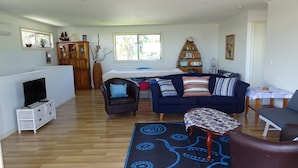 Amplia sala de estar con un sofá azul, una mesita y un televisor sobre un mueble blanco.