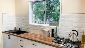 Une cuisine moderne avec une fenêtre, des meubles blancs, un plan de travail en bois, une cuisinière à gaz et une bouilloire.