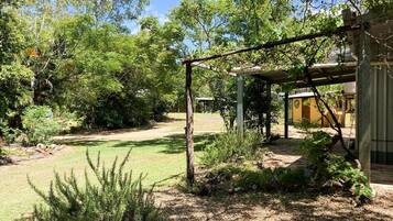 Um jardim com pérgola de madeira, gramado e um edifício com fachada amarela.