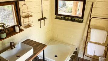 Un baño con tocador de madera, lavamanos blanco, ducha y perchero para toallas.