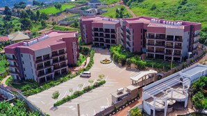 A multi-story hotel with a parking lot, surrounded by greenery and hills. - Sand Grains Residences 002 (Entebbe)