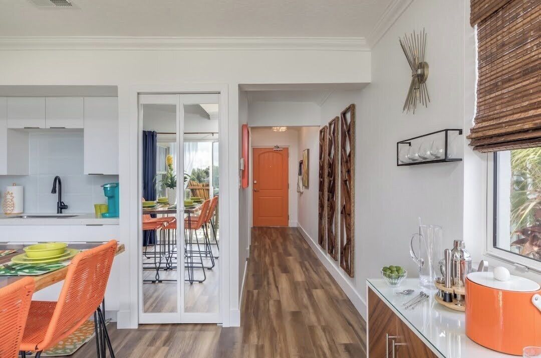 A modern kitchen with white cabinets, a dining area with orange chairs, and a wooden floor.