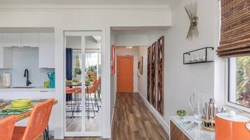 A modern kitchen with white cabinets, a dining area with orange chairs, and a wooden floor.