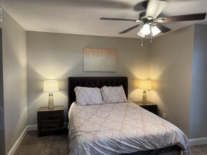 Una camera da letto con un letto, due lampade da comodino, una ventola a soffitto e un'opera d'arte appesa al muro.