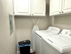 A laundry room with two white washing machines, a dryer, and a utility meter on the wall.