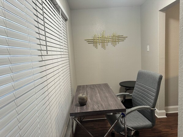 Une petite salle de réunion comprenant une table, une chaise, un élément décoratif mural et une fenêtre avec des stores.