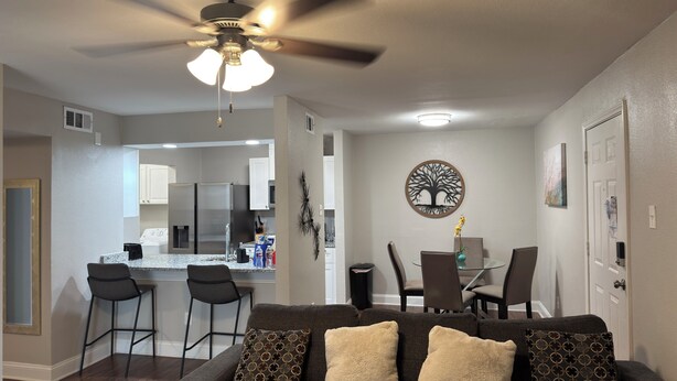 A modern living room with a dark brown sofa, a ceiling fan, and a dining area with a glass table and chairs. - I042 – Upgraded 2BD Apt | Pool | DFW South 183/161 (Irving)