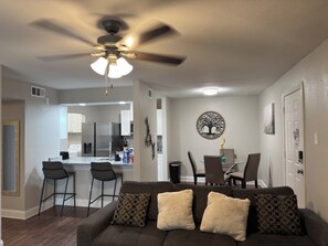 A modern living room with a dark brown sofa, a ceiling fan, and a dining area with a glass table and chairs.