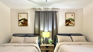 Habitación de hotel con dos camas, una mesita de noche con lámpara y dos cuadros colgados en la pared.