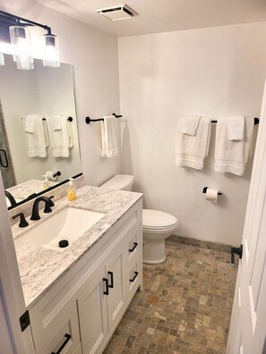 A bathroom with a white sink, black faucet, and a marble countertop. There are white towels hanging on a rack, and a toilet with a roll of toilet paper on the wall. - "Two-Story Townhome Newly Renovated One-Bedroom Getaway Awaits Your Stay!" (Tucson)