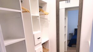 Un pasillo con un armario blanco, piso de madera y un espejo en la pared.