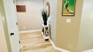 A hallway with wooden flooring, a white door, a small white console table with a plant, and a framed picture on the wall. - EastGate 4A Cozy family retreat close to downtown Hammond (Hammond)
