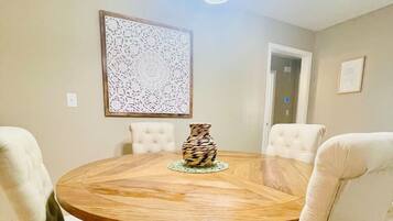 Una mesa de comedor redonda de madera con cuatro sillas tapizadas, un jarrón decorativo y una araña.