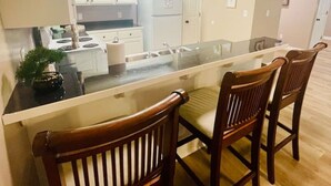 A modern kitchen with white cabinets, a stainless steel refrigerator, and a glass island with wooden chairs. - EastGate 4A Cozy family retreat close to downtown Hammond (Hammond)